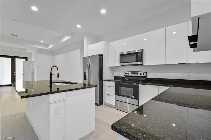 Kitchen featuring appliances with stainless steel finishes, recessed lighting, a center island with sink, dark stone counters, and white cabinets