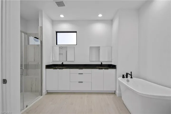 Full bath featuring a marble finish shower, double vanity, a freestanding bath, light wood-style flooring, and recessed lighting