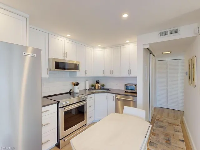 Kitchen featuring light hardwood / wood-style floors, appliances with stainless steel finishes, decorative backsplash, and white cabinets