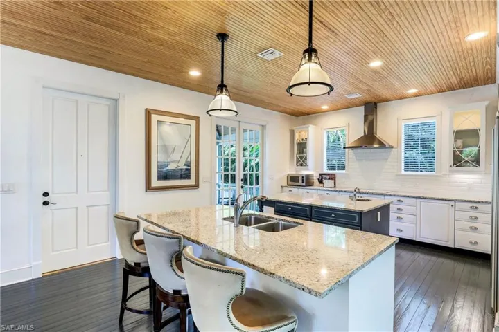 Kitchen featuring tasteful backsplash, white cabinetry, pendant lighting, light stone countertops, and dark wood finished floors