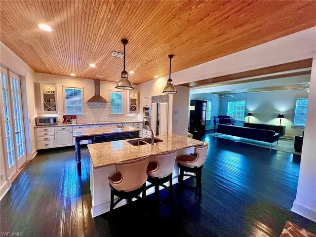 Kitchen featuring decorative light fixtures, a breakfast bar, light stone countertops, backsplash, and wall chimney range hood