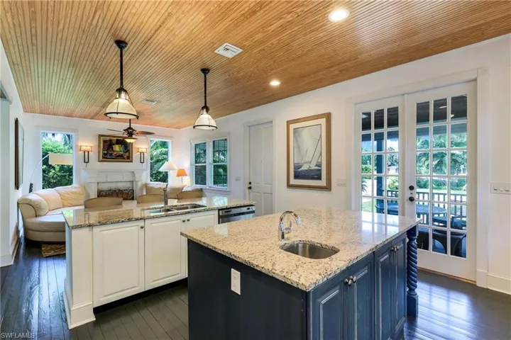 Kitchen featuring a center island with sink, french doors, light stone countertops, white cabinets, and decorative light fixtures