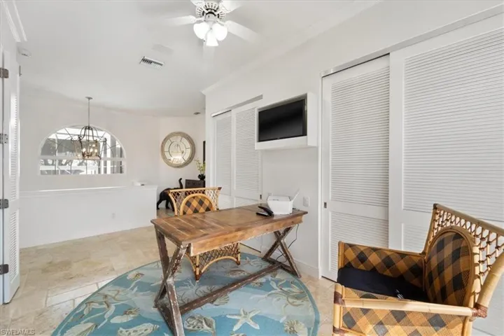 Home office with ornamental molding, a ceiling fan, light stone finish flooring, and a chandelier