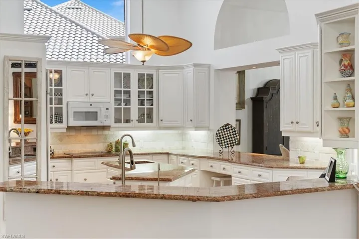 Kitchen with backsplash, open shelves, light stone counters, white microwave, and a high ceiling