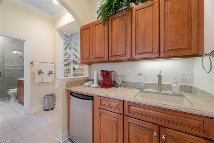Kitchen featuring stainless steel refrigerator, brown cabinets, light stone counters, ornamental molding, and arched walkways