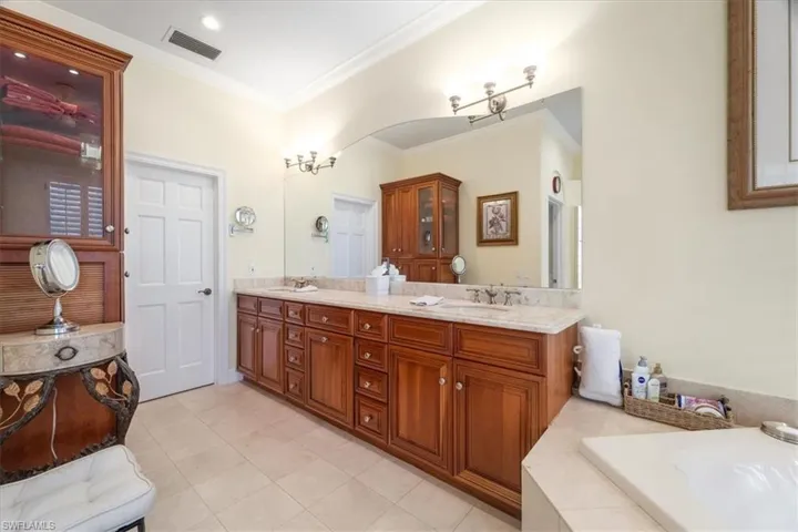 Full bathroom featuring double vanity, light tile patterned floors, crown molding, and tiled tub