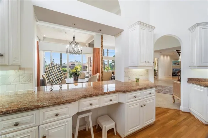 Kitchen with decorative backsplash, light wood finished floors, dark stone countertops, white cabinets, and hanging light fixtures