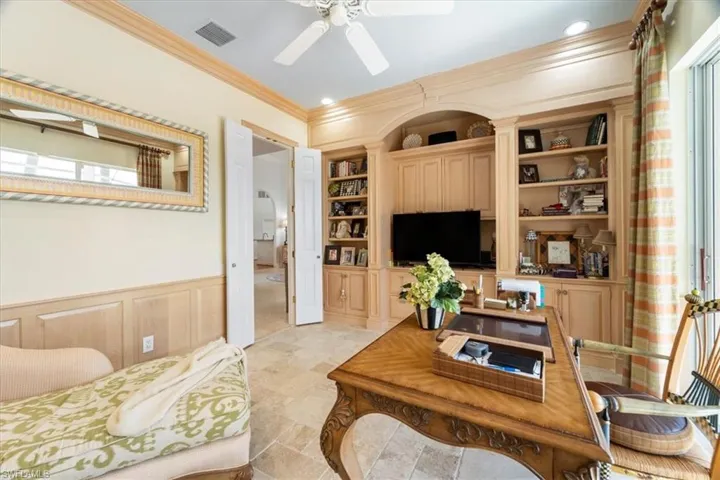Office space with built in features, a wainscoted wall, ornamental molding, a ceiling fan, and a decorative wall