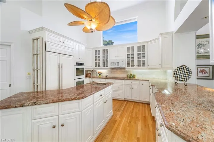 Kitchen featuring tasteful backsplash, glass insert cabinets, light wood-style flooring, dark stone countertops, and white cabinets