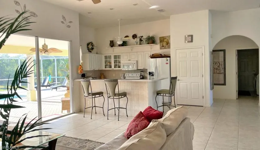 Kitchen featuring light tile flooring, ceiling fan, kitchen peninsula, and white appliances