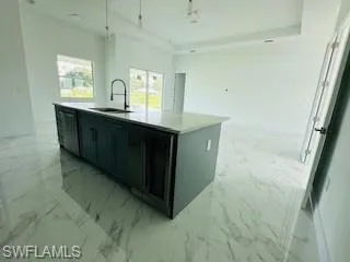 Kitchen with light tile patterned flooring, black dishwasher, a kitchen island with sink, and sink