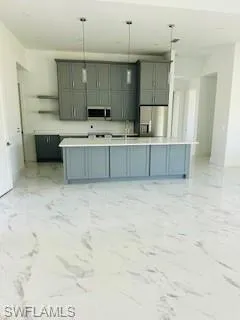 Kitchen with gray cabinets, stainless steel appliances, light tile patterned floors, and an island with sink