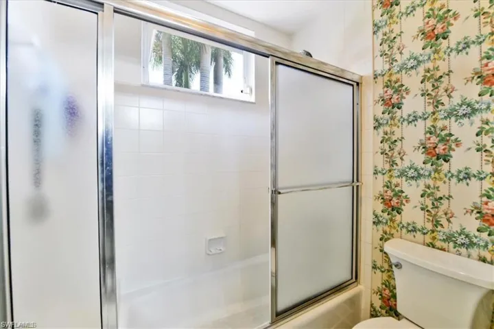 Bathroom with bath / shower combo with glass door and toilet