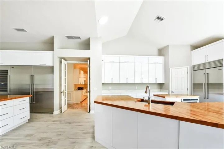 Kitchen with wooden counters, white cabinets, stainless steel built in fridge, and light wood-type flooring
