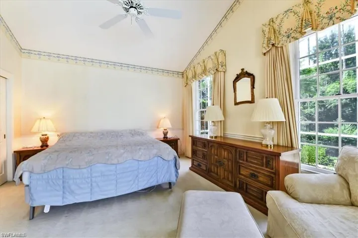 Carpeted bedroom featuring vaulted ceiling, ornamental molding, ceiling fan, and multiple windows