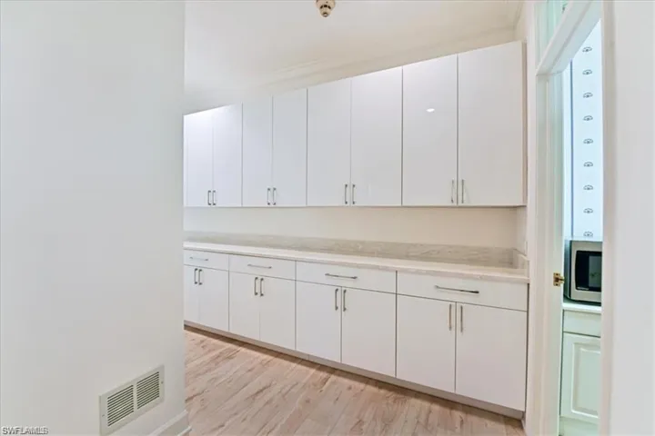 Kitchen with white cabinets, stainless steel microwave, and light hardwood / wood-style flooring