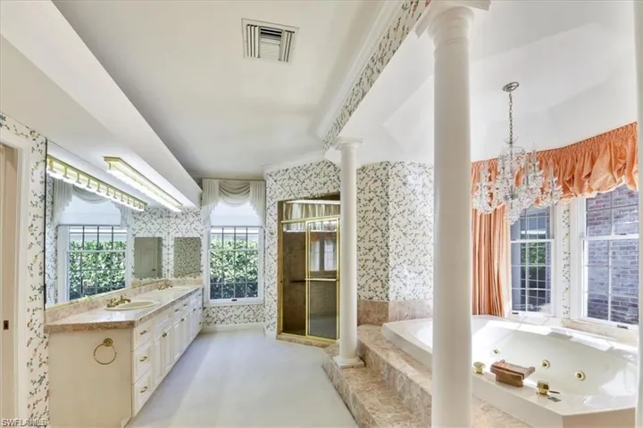 Bathroom with plus walk in shower, an inviting chandelier, decorative columns, and vanity