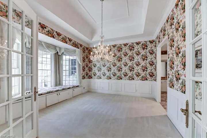 Carpeted empty room with an inviting chandelier, a tray ceiling, and french doors
