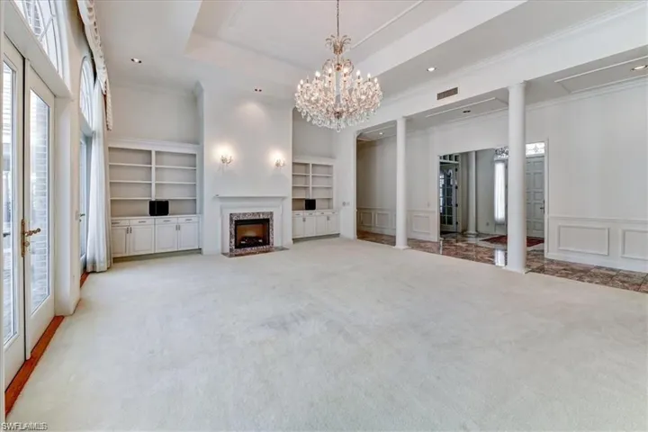 Unfurnished living room with a chandelier, built in features, a tray ceiling, ornate columns, and a high end fireplace