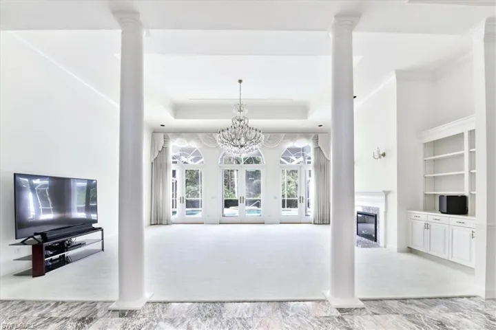 Carpeted living room featuring ornate columns, a chandelier, a high end fireplace, and a tray ceiling