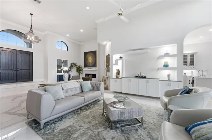 Living area with a high ceiling, crown molding, light marble finish flooring, hanging lights, and ceiling fan