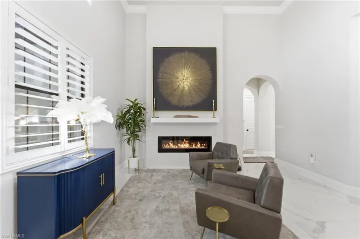 Sitting room featuring a glass covered fireplace, crown molding, marble finish floors, and arched walkways