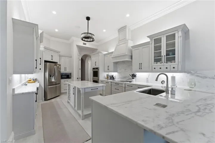 Kitchen featuring glass fronted cabinets, arched walkways, white cabinets, a center island, and stainless steel appliances