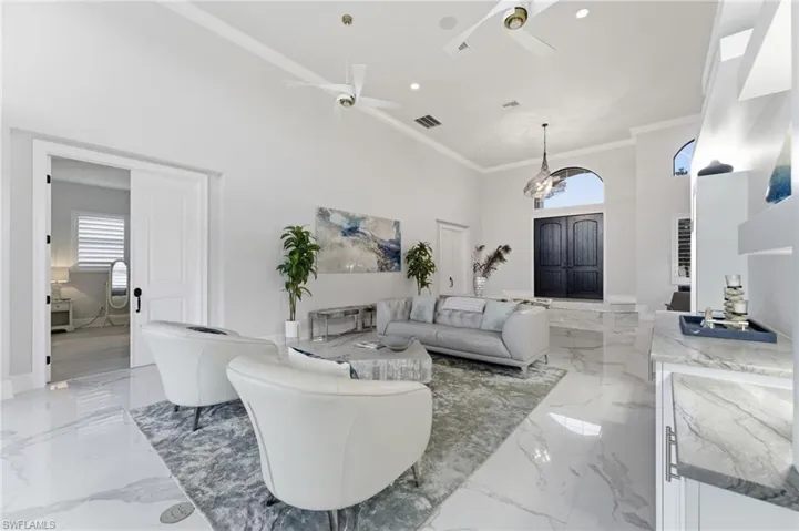 Living area with a high ceiling, healthy amount of natural light, crown molding, ceiling fan, and light marble finish flooring
