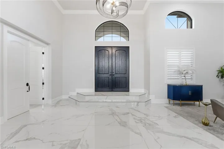 Foyer entrance featuring hanging lights, a high ceiling, crown molding, and light marble finish flooring