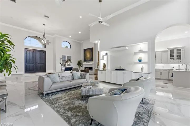 Living room featuring light marble finish flooring, crown molding, a high ceiling, a ceiling fan, and suspended lighting