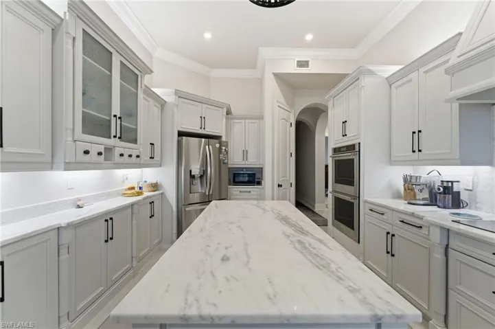 Kitchen featuring light stone counters, arched walkways, glass insert cabinets, stainless steel appliances, and ornamental molding