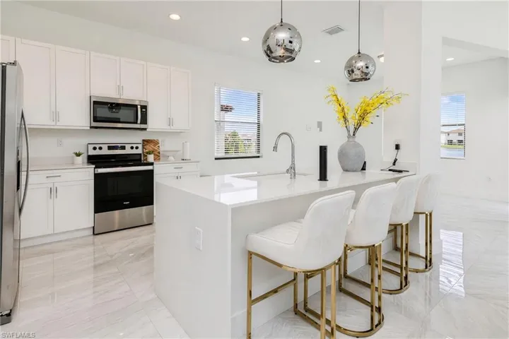Kitchen featuring stainless steel appliances, white cabinetry, a large center island with a sink, and polished tile flooring