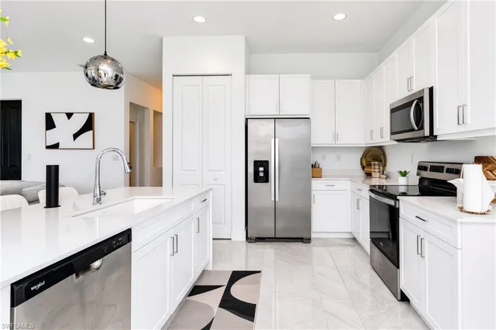 White cabinetry with brushed nickel hardware, stainless steel appliances, a large center island with an integrated sink, white countertops, and light-toned tile flooring