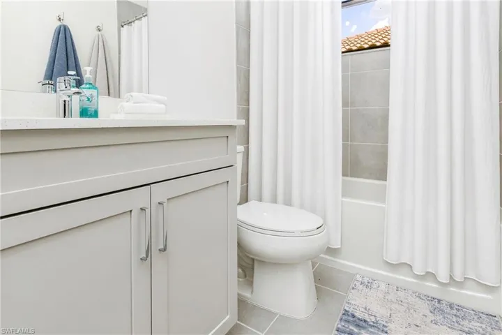 White vanity with a light-colored countertop, chrome faucet, and tiled shower surround