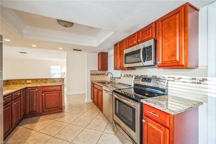 Kitchen featuring stainless steel appliances, sink, a raised ceiling, light stone counters, and crown molding