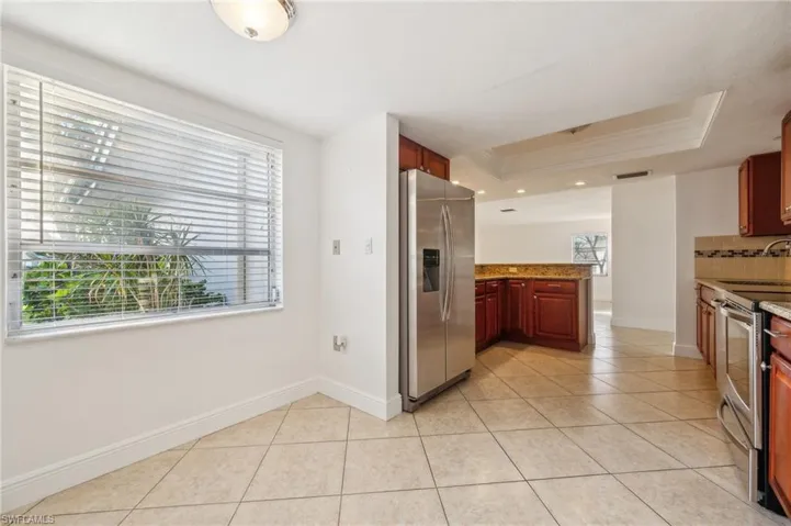 Kitchen with appliances with stainless steel finishes, plenty of natural light, a raised ceiling, kitchen peninsula, and light stone counters
