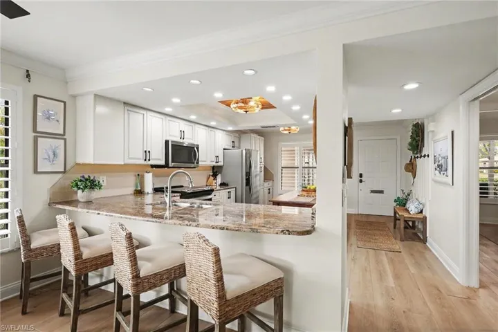 Kitchen featuring light wood-style floors, white cabinetry, light stone counters, crown molding, and a kitchen bar