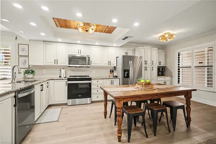 Kitchen featuring stainless steel appliances, light stone counters, light wood-type flooring, white cabinets, and ornamental molding