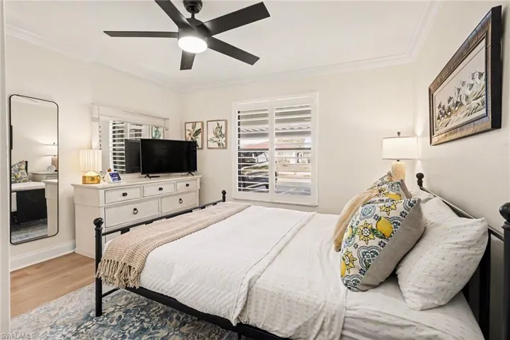 Bedroom with wood finished floors, crown molding, ceiling fan, and multiple windows