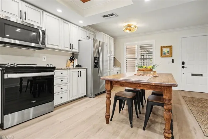 Kitchen featuring stainless steel appliances, ornamental molding, white cabinets, light wood-type flooring, and light stone counters
