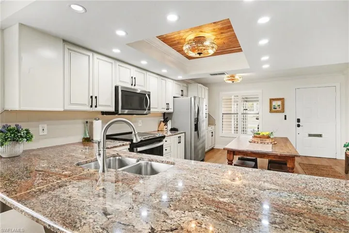 Kitchen with crown molding, white cabinets, light stone counters, light wood-type flooring, and stainless steel appliances