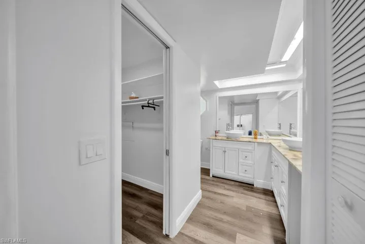 Full bathroom featuring double vanity, a walk in closet, and light wood-style floors