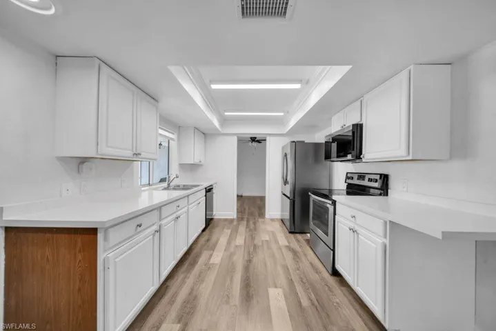 Kitchen featuring stainless steel appliances, white cabinets, a raised ceiling, and light countertops