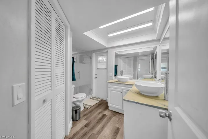 Bathroom featuring a closet, vanity, light wood finished floors, a shower stall, and a raised ceiling