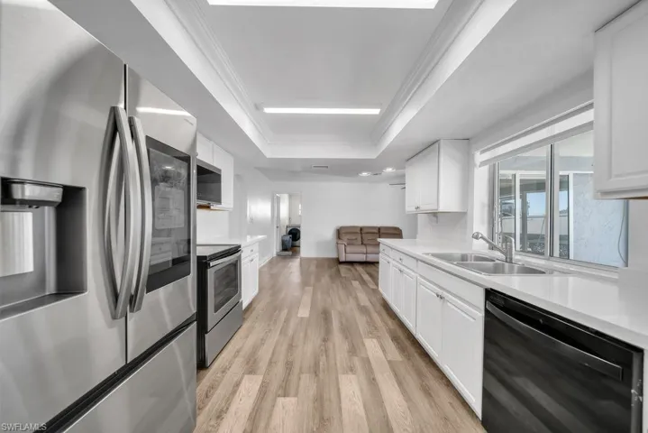 Kitchen with stainless steel appliances, white cabinetry, light wood-type flooring, crown molding, and a tray ceiling