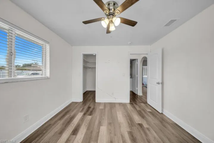 Unfurnished bedroom featuring a walk in closet, light wood-type flooring, a ceiling fan, and arched walkways