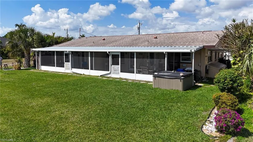 Rear view of house with a yard, roof with shingles, a sunroom, and a hot tub