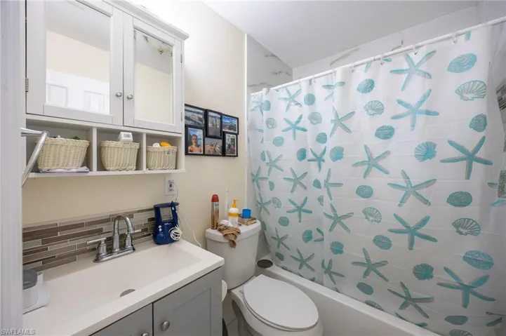 Bathroom with toilet, decorative backsplash, shower / bath combination with curtain, and vanity