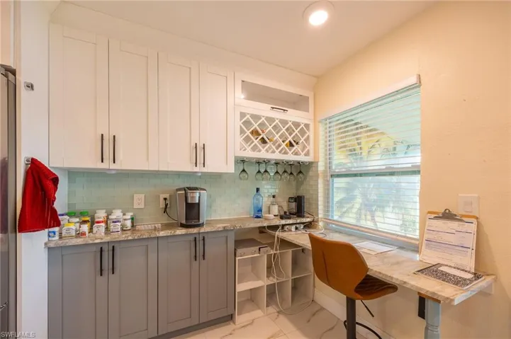 Kitchen featuring marble finish floor, light stone countertops, white cabinets, and decorative backsplash