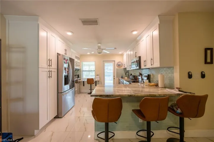 Kitchen with white cabinets, appliances with stainless steel finishes, a peninsula, marble finish floor, and light stone countertops